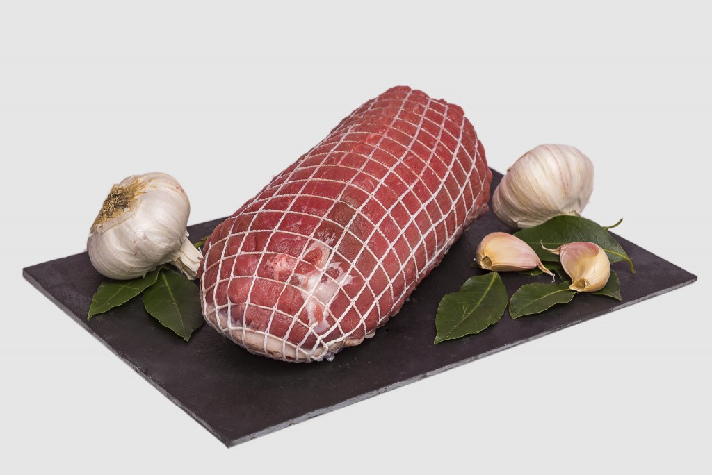 Pieza de carne atada con malla elástica alimentaria junto a ajos y laurel